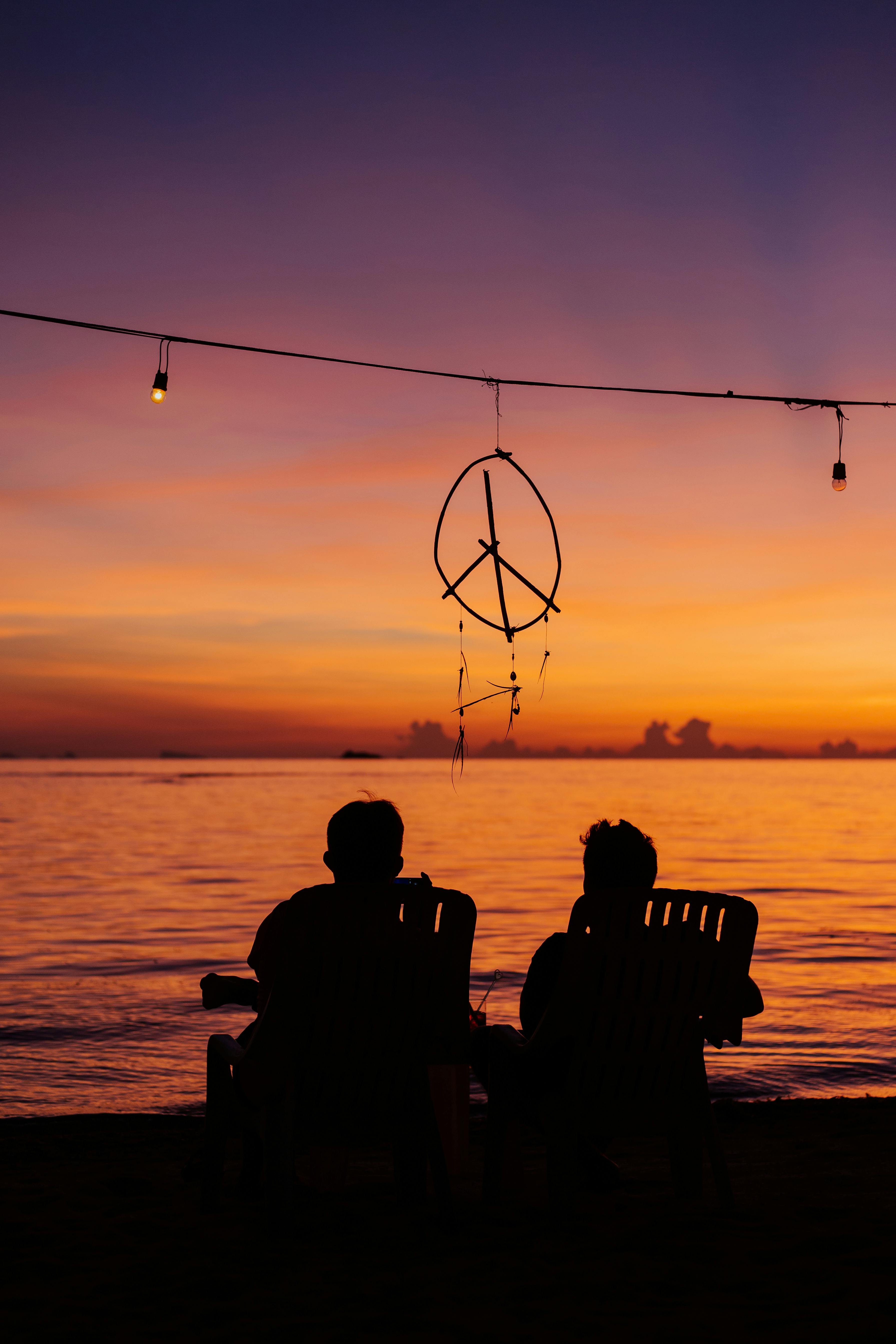 silhouette of two people sitting on the beach during golden hour