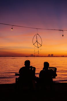 Silhouettes of two people sitting by the sea during a vibrant sunset, creating a peaceful ambiance.