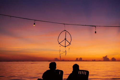 Free Two people enjoying a serene sunset by the sea with a hanging dreamcatcher Stock Photo