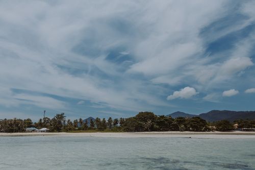 Free Serene tropical beach scene with palm trees, mountains, and a vibrant blue sky. Stock Photo