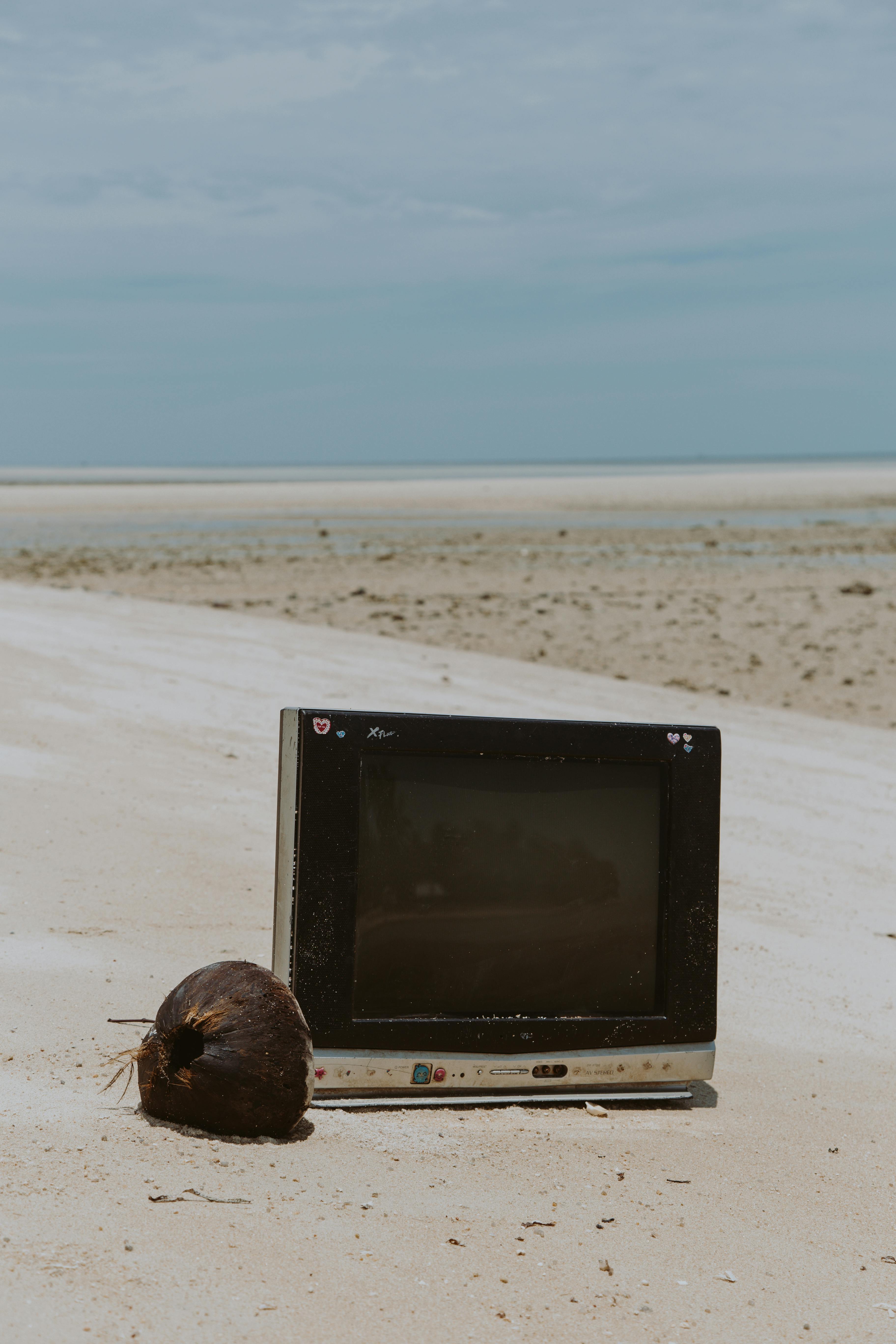 an old tv and a coconut lying on the sand on the beach