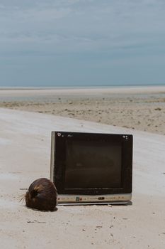 在一个空旷宁静的海滩场景中，一台复古电视机旁放着一个椰子