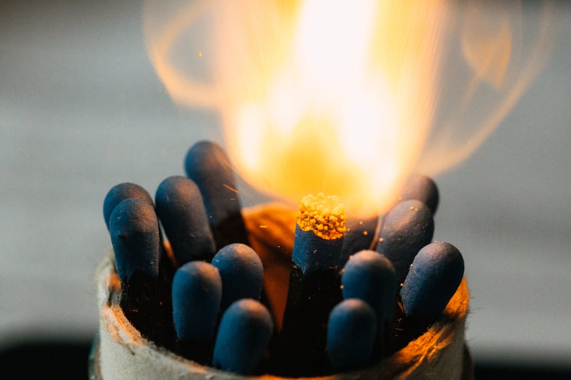 Closeup of burning fire on match head among pile of black matches in jar on blurred background