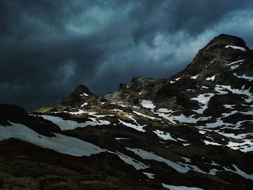 Majestic view of mountain range covered with snow against cloudy sky in dark in overcast weather in nature in winter