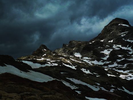 Majestic view of mountain range covered with snow against cloudy sky in dark in overcast weather in nature in winter