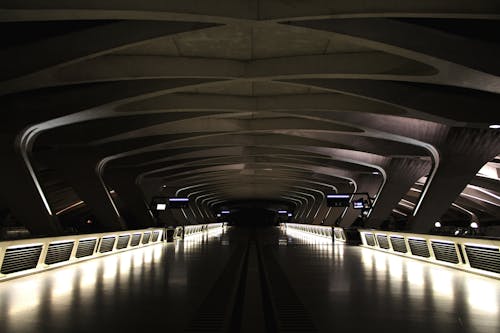 Perspective view of modern dark empty train station with illuminated sides of walkway and futuristic ceiling in night time inside