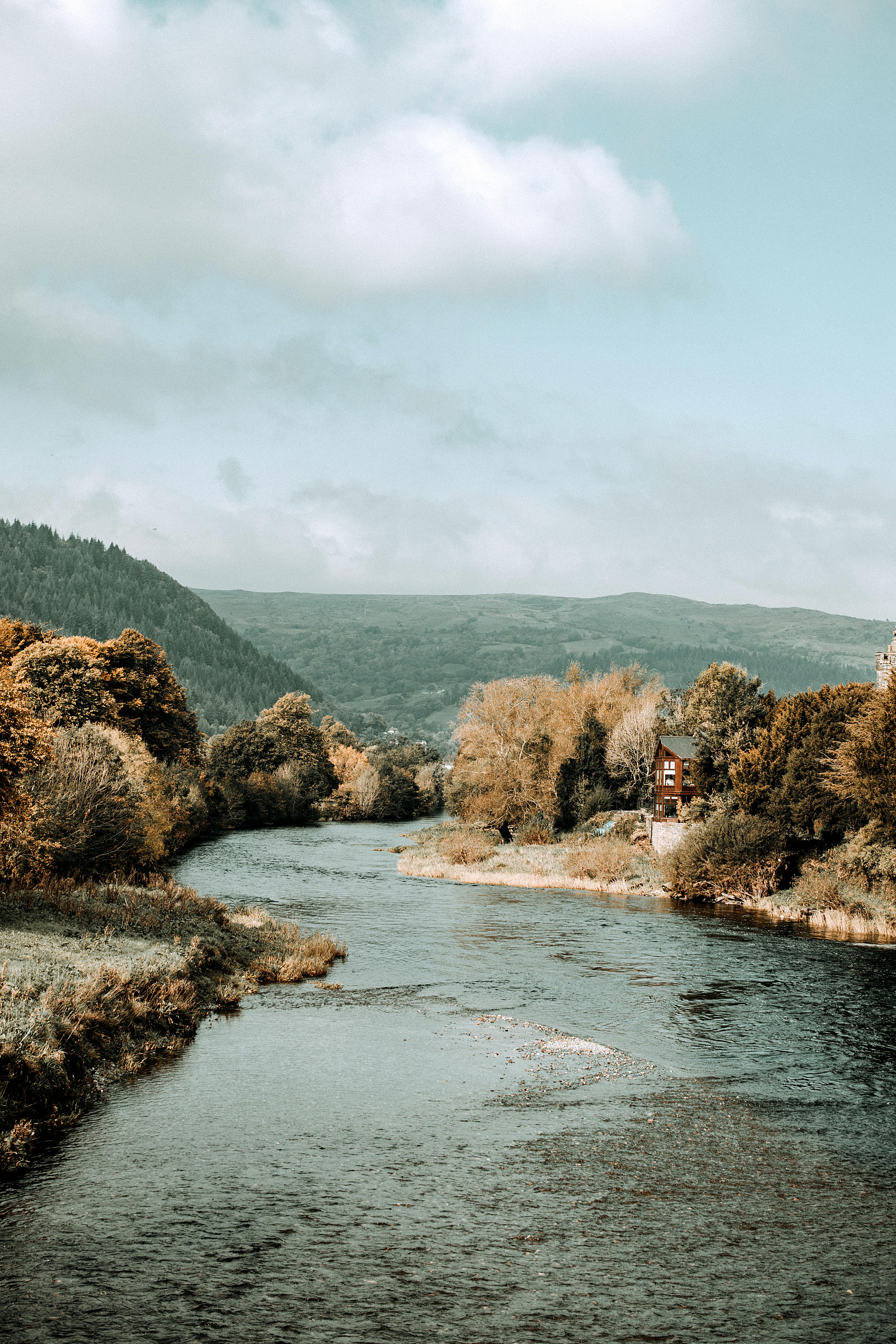 A scenic river view in Llanrwst, Wales with lush trees and distant mountains.