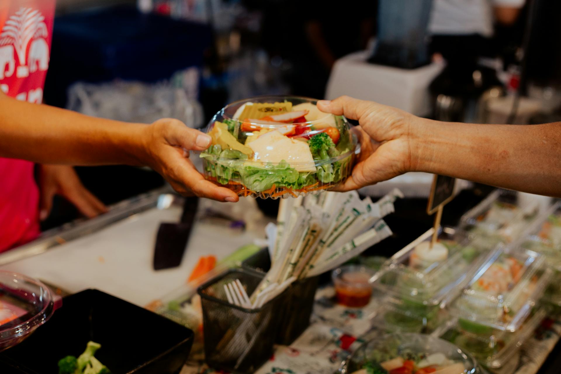 Person Handing Over A Packed Vegetable Salad in Plastic Container