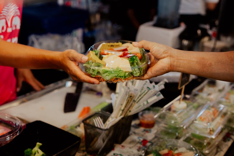 Person Handing Over A Packed Vegetable Salad In Plastic Container 