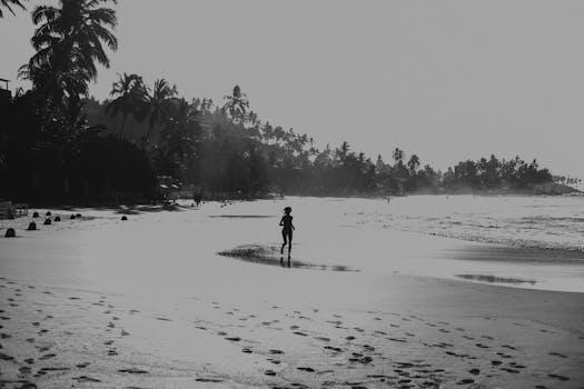 A woman runs along Mirissa Beach, Sri Lanka, silhouetted against the sky in a black and white photo.