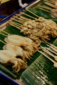 Close-up of grilled squid skewers on banana leaves at a Thai street food market.
