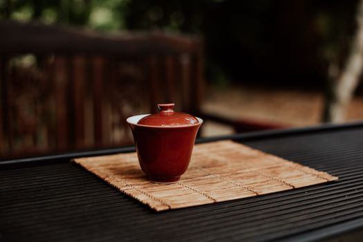 一个红色陶瓷杯优雅地置于木桌上的竹制餐垫上，营造出极简主义的静物氛围