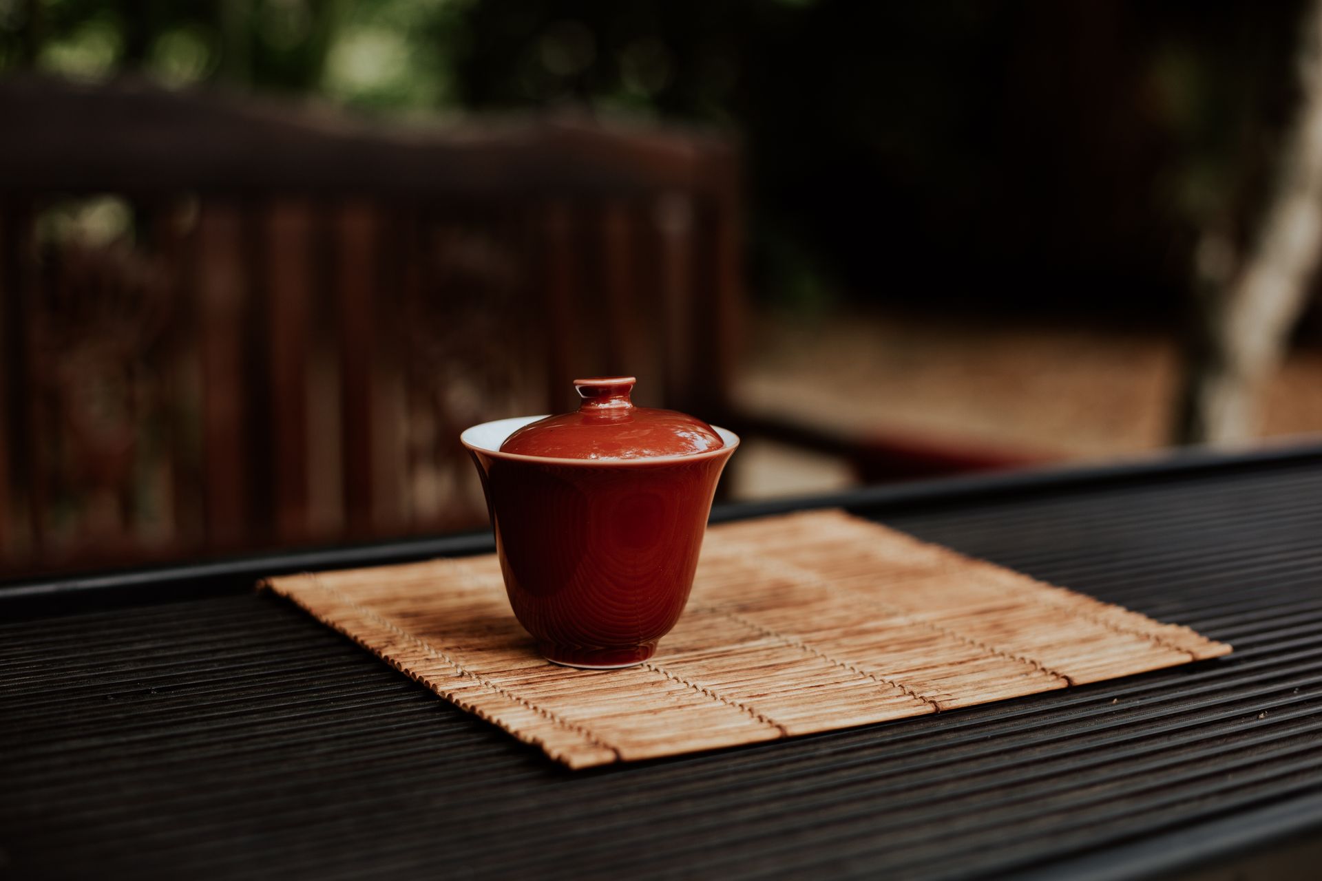 A red ceramic cup sits elegantly on a bamboo placemat on a wooden table, creating a minimalist still life.