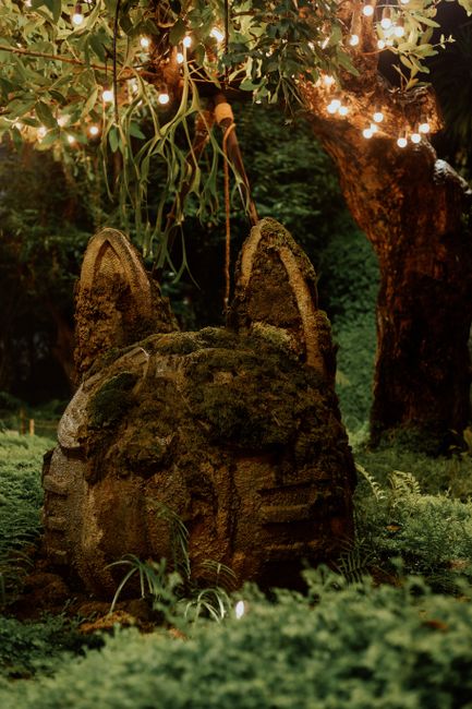 Moss-covered stone sculpture in a magical forest with glowing tree lights creating an enchanting atmosphere.