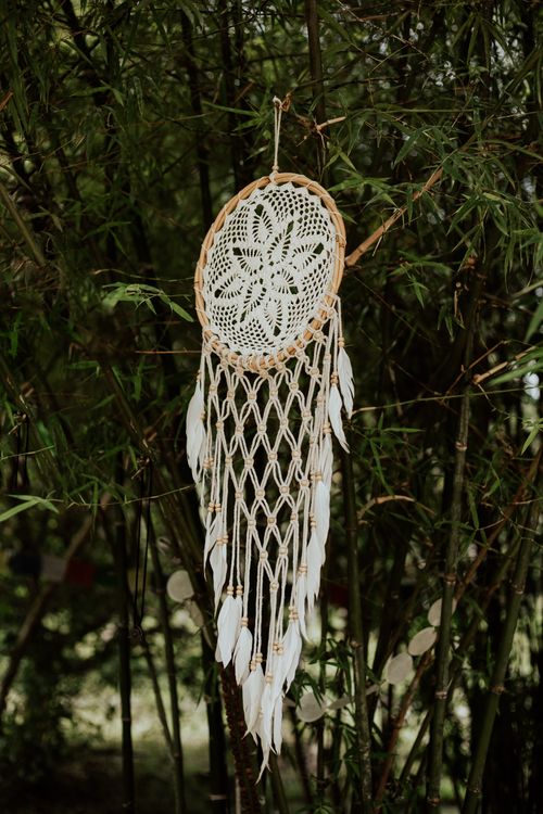 Free A beautifully handcrafted dream catcher hangs among lush green branches, capturing the essence of summer. Stock Photo