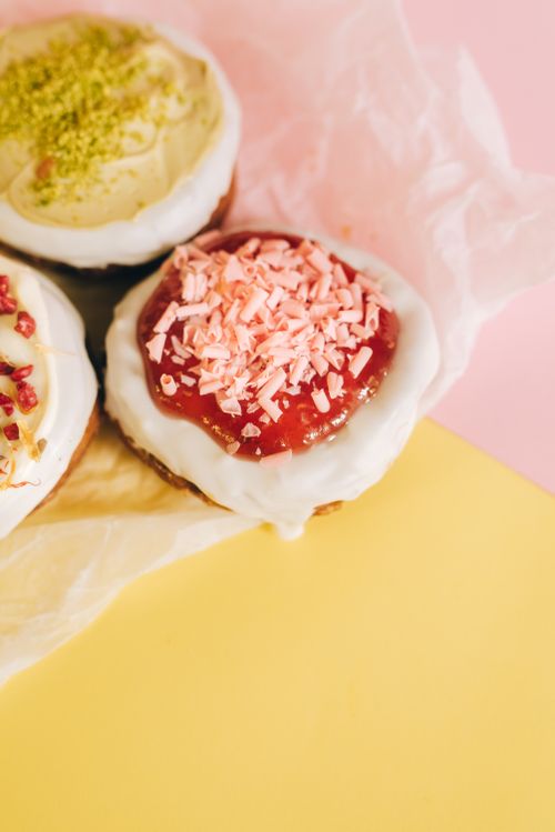 Free Vibrant close-up of assorted iced donuts with pink sprinkles on pastel paper surface. Stock Photo