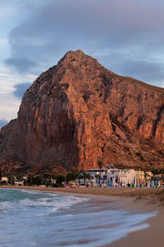 Stunning view of San Vito Lo Capo's beach with towering mountain during golden hour.