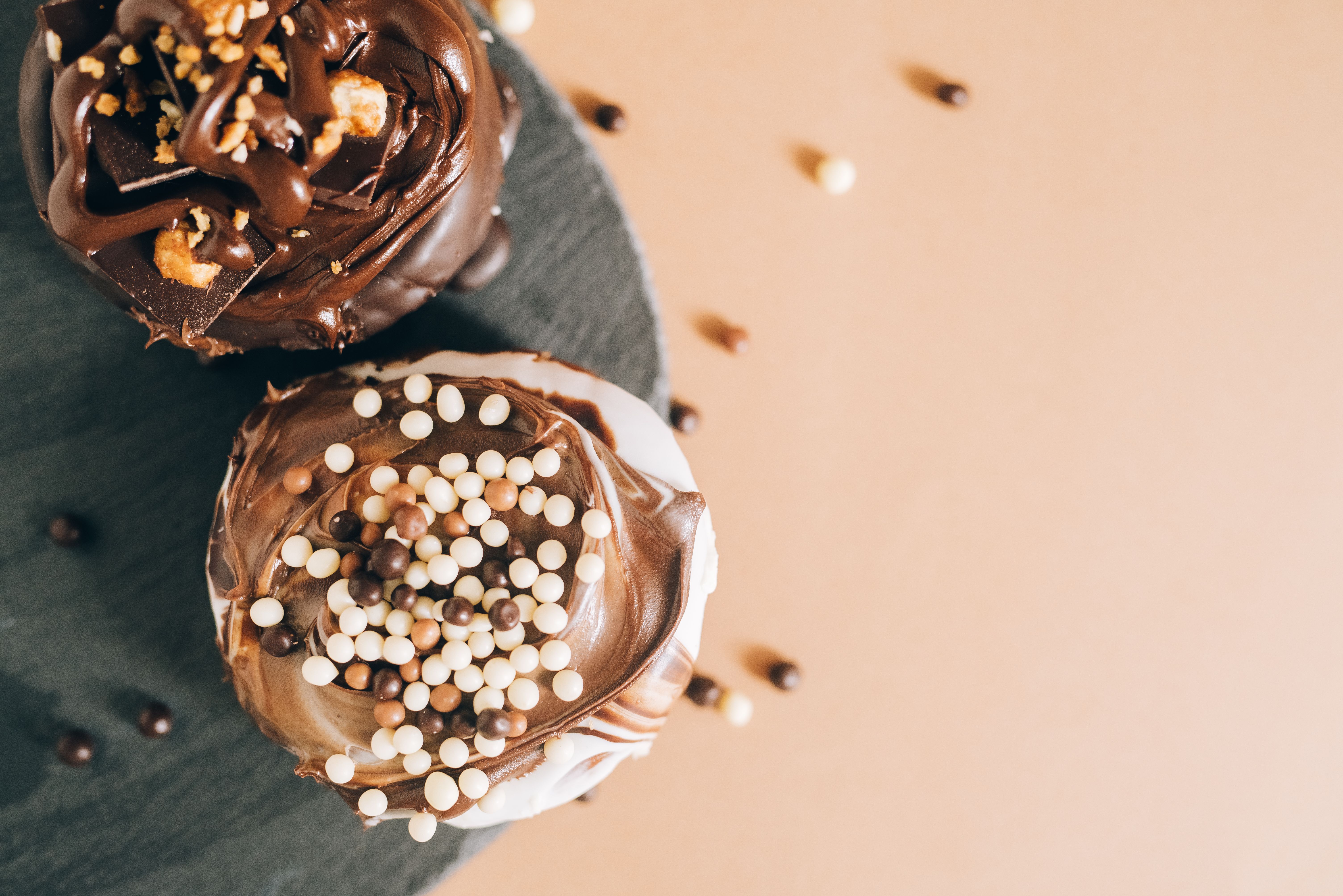 Top view of two chocolate cupcakes with cream and sprinkles on a plate.