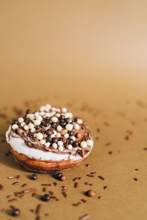 Free A close-up of a cronut topped with chocolate sprinkles on a brown background, perfect for dessert lovers. Stock Photo