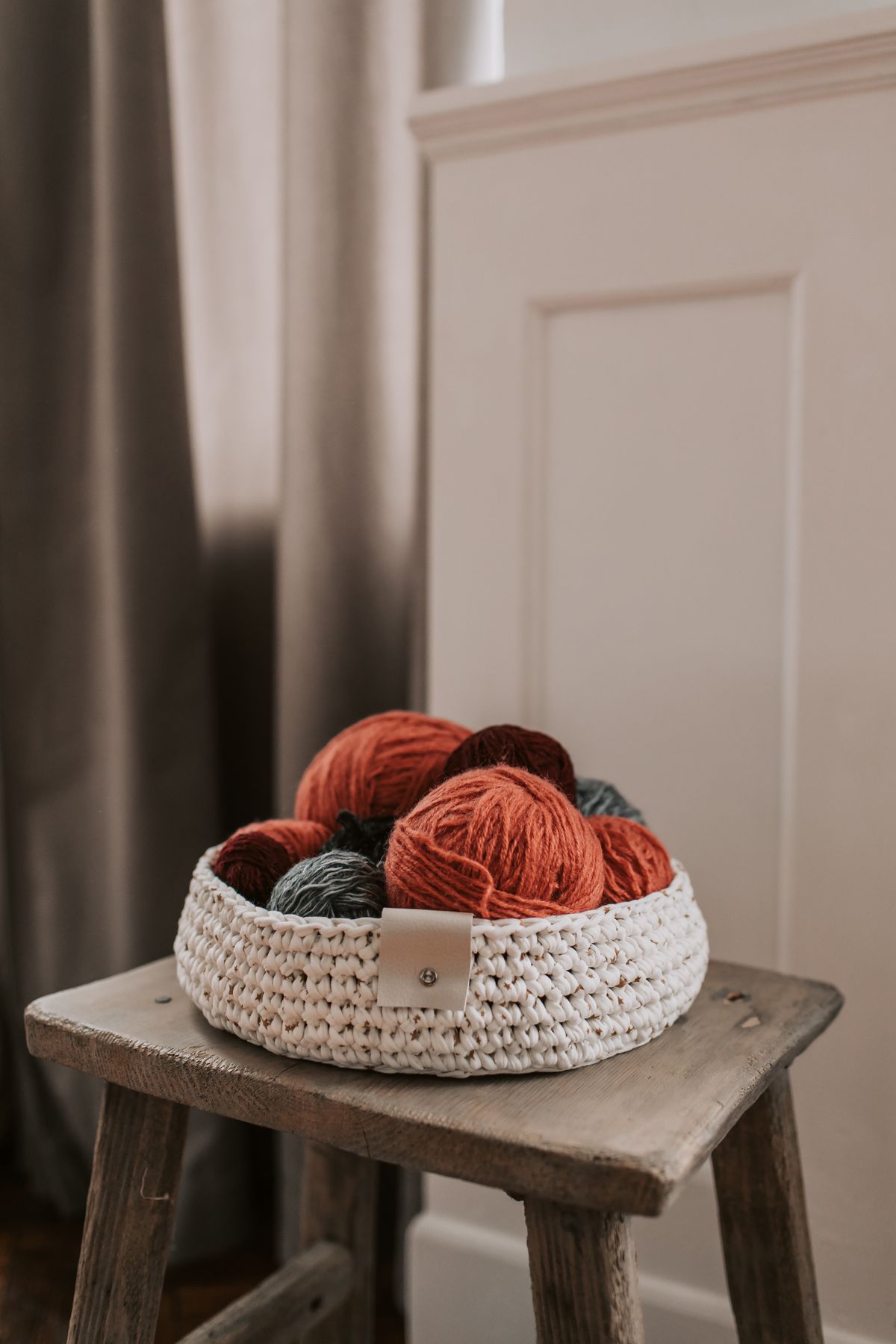 A crocheted basket holding yarn on a wooden stool