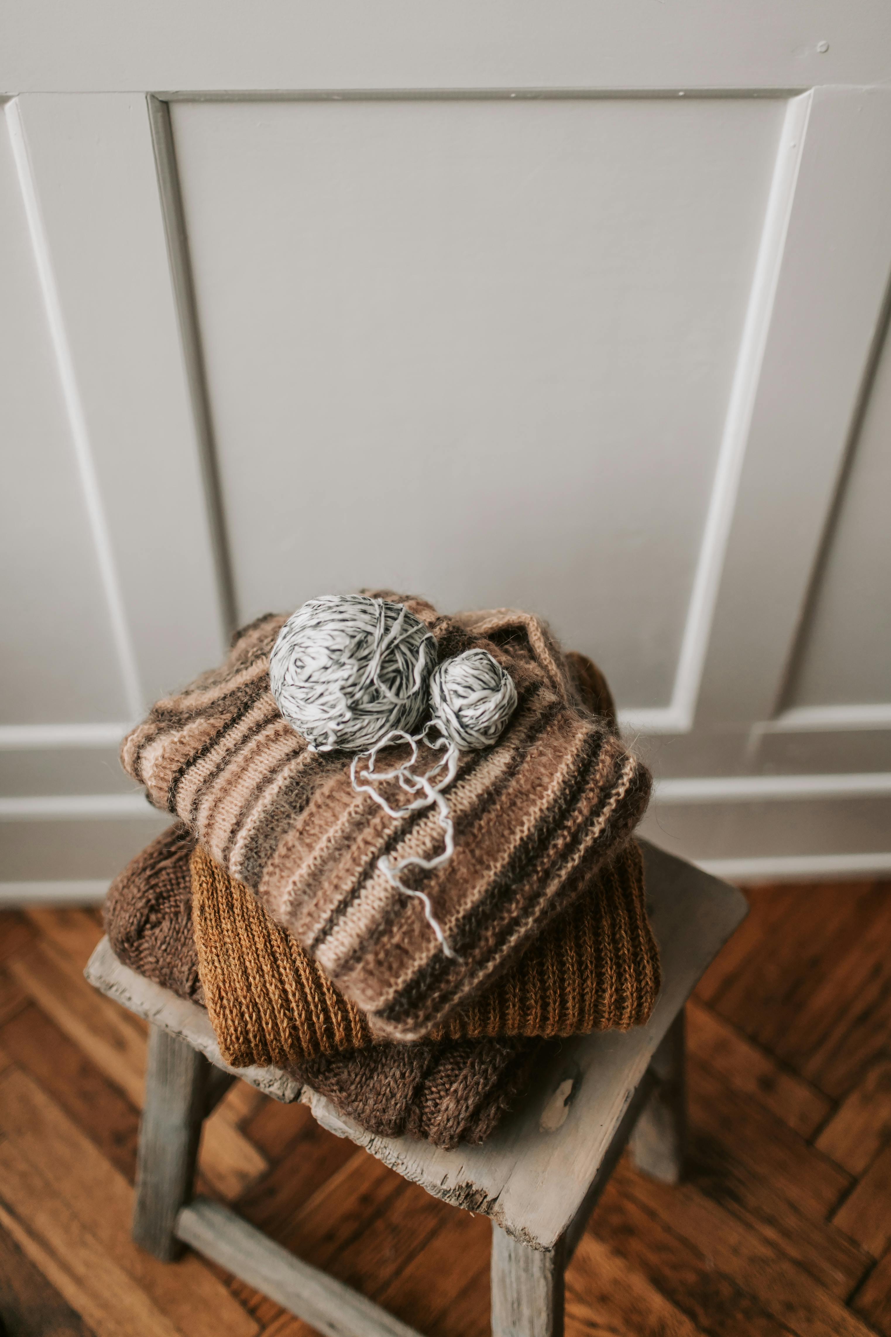 质朴的凳子上放着一堆手工针织的温暖毛衣，毛衣上还有纱线