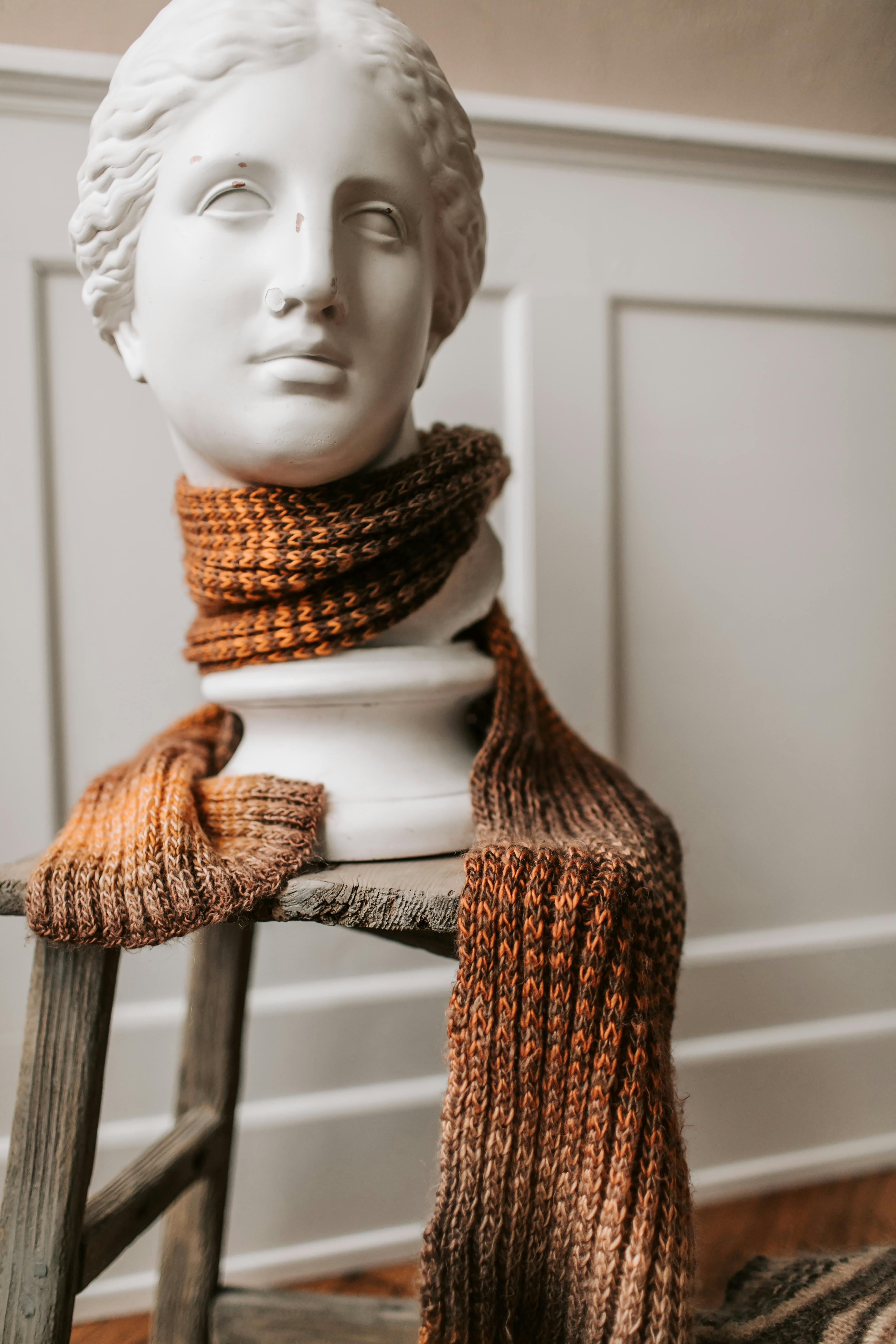 室内乡村木凳上的大理石半身像，装饰着一条温暖的针织围巾
