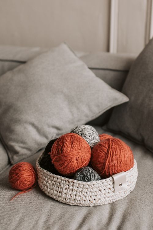 Free Warm orange and gray yarn balls in a knitted basket on a cozy sofa. Stock Photo