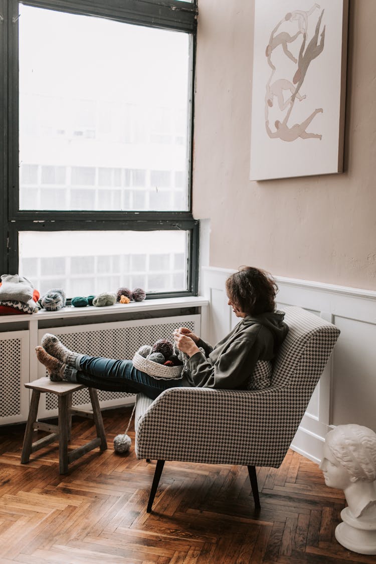 A Woman Knitting While Sitting On Padded Armchair