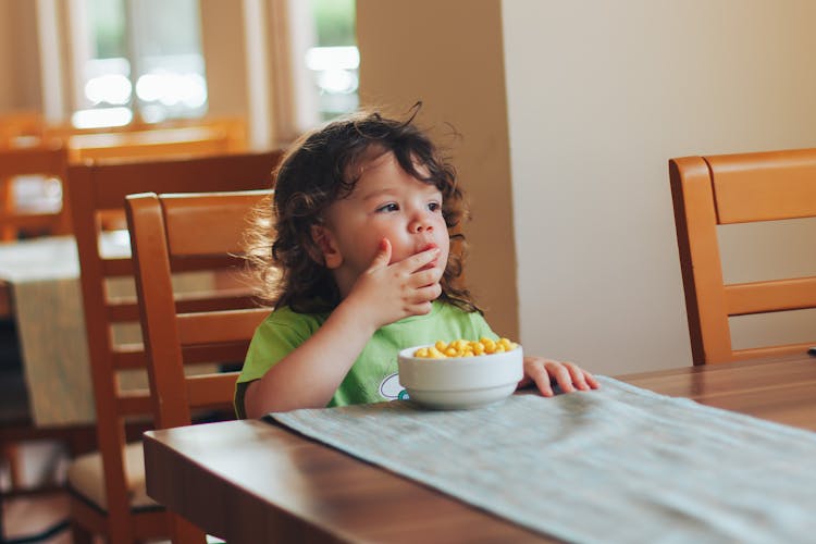 Child Sitting At Table Eating Breakfast