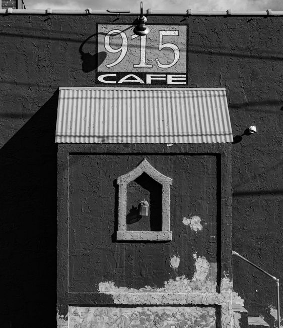 Black and white of wall with number and shabby entrance to aged cafe in sunlight in city