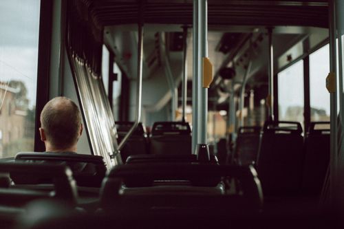 Free Back view of anonymous male riding on empty bus while sitting on passenger seat near window during trip in city street Stock Photo