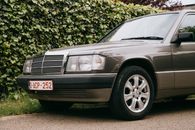 Grey automobile with small transparent rectangular headlights and glossy surface parked on road near hedge in daytime