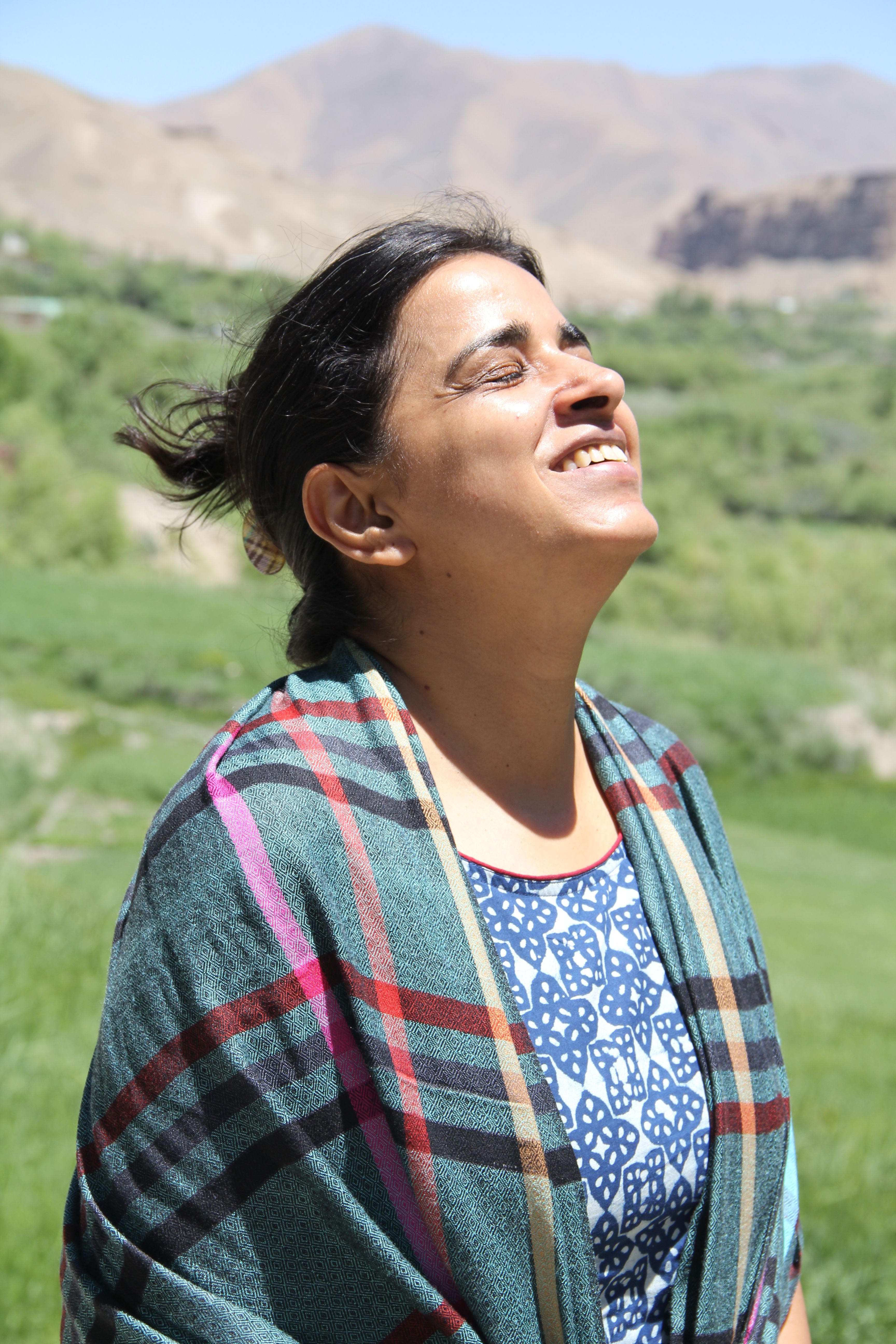 Woman with closed eyes smiling under the sun in a green outdoor setting.