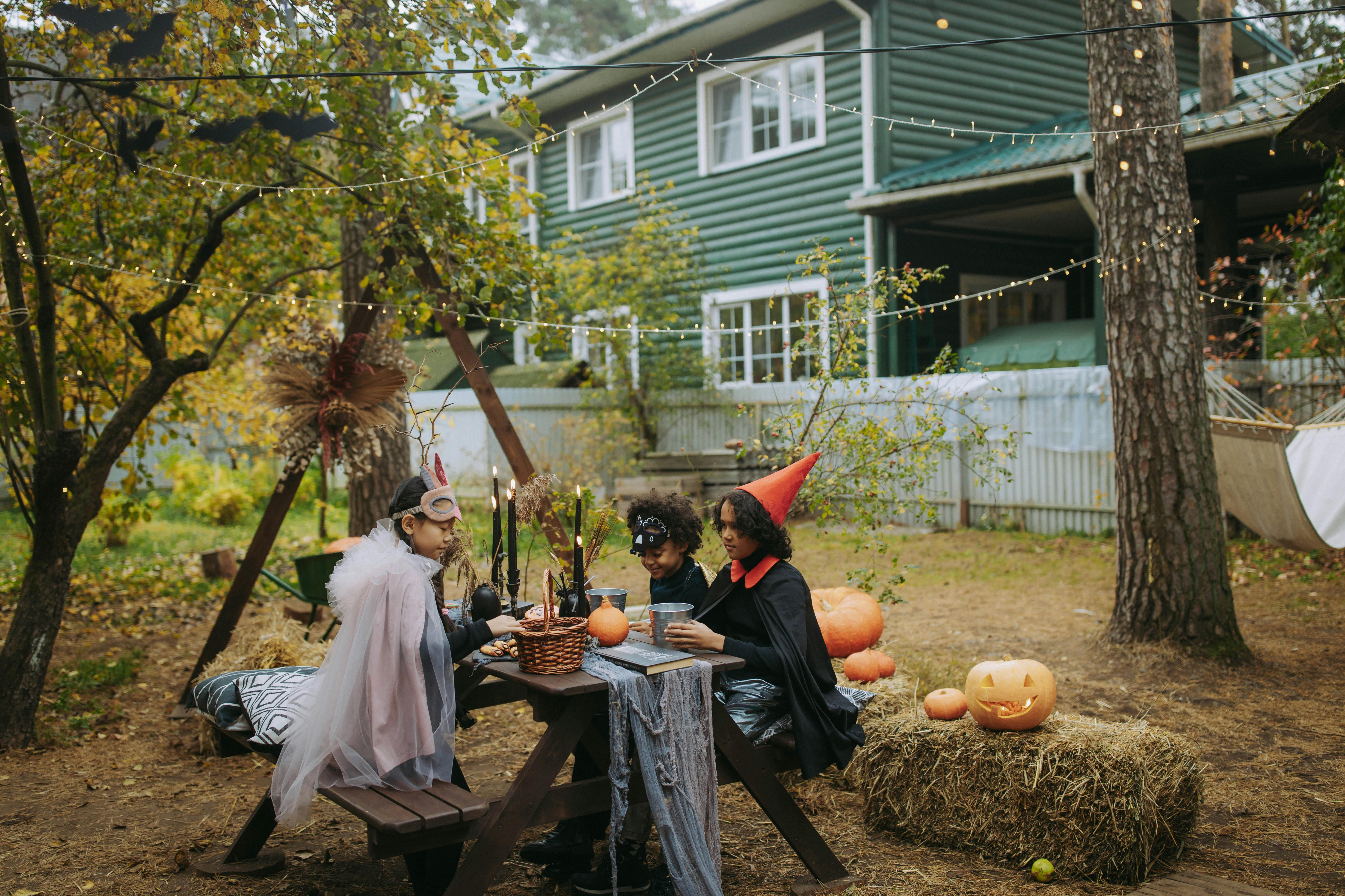 Group of children in Halloween costumes enjoying a festive backyard setup with pumpkins and decorations.