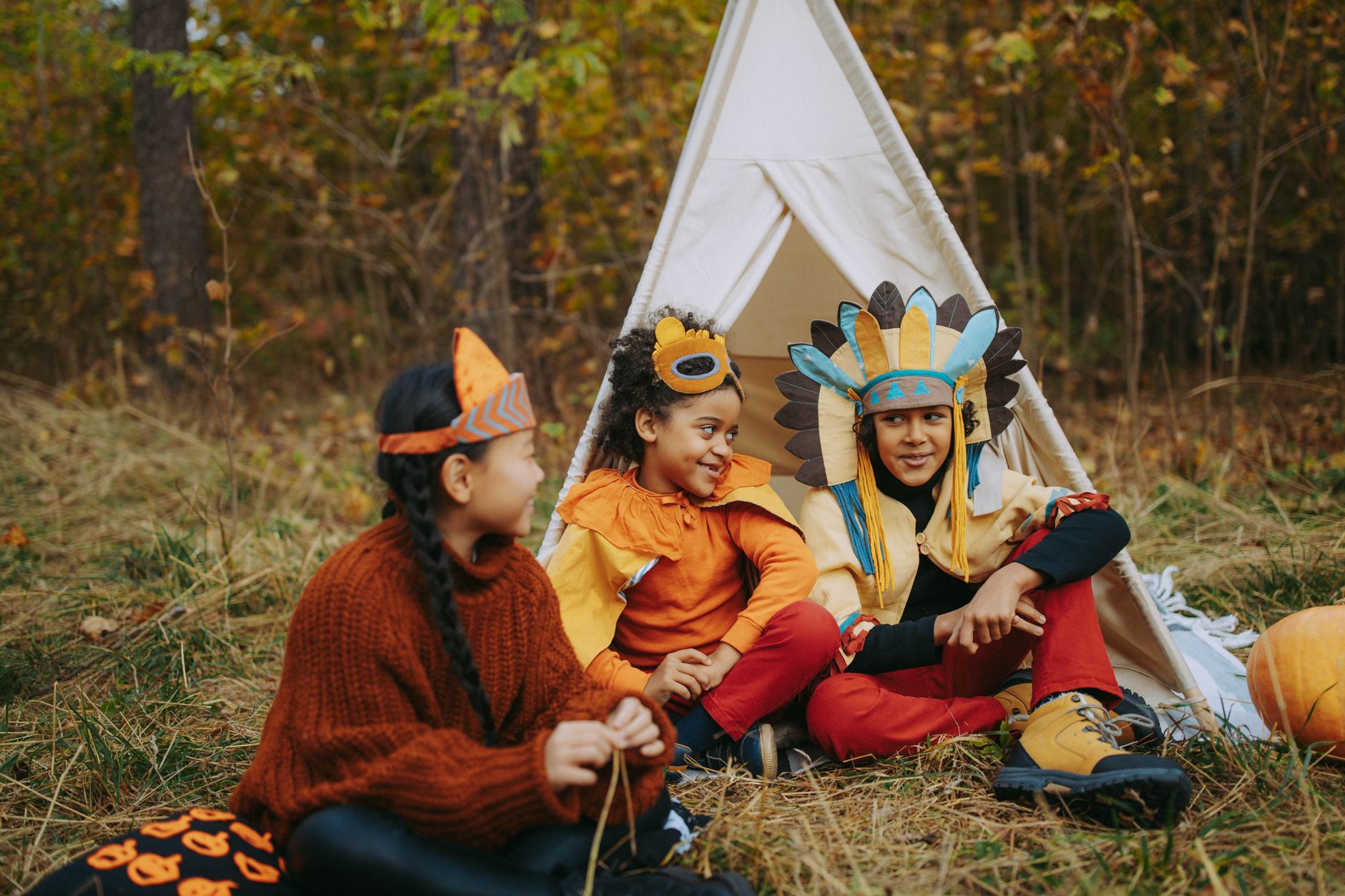 Three kids in vibrant costumes enjoying a fun day outdoors near a teepee tent.
