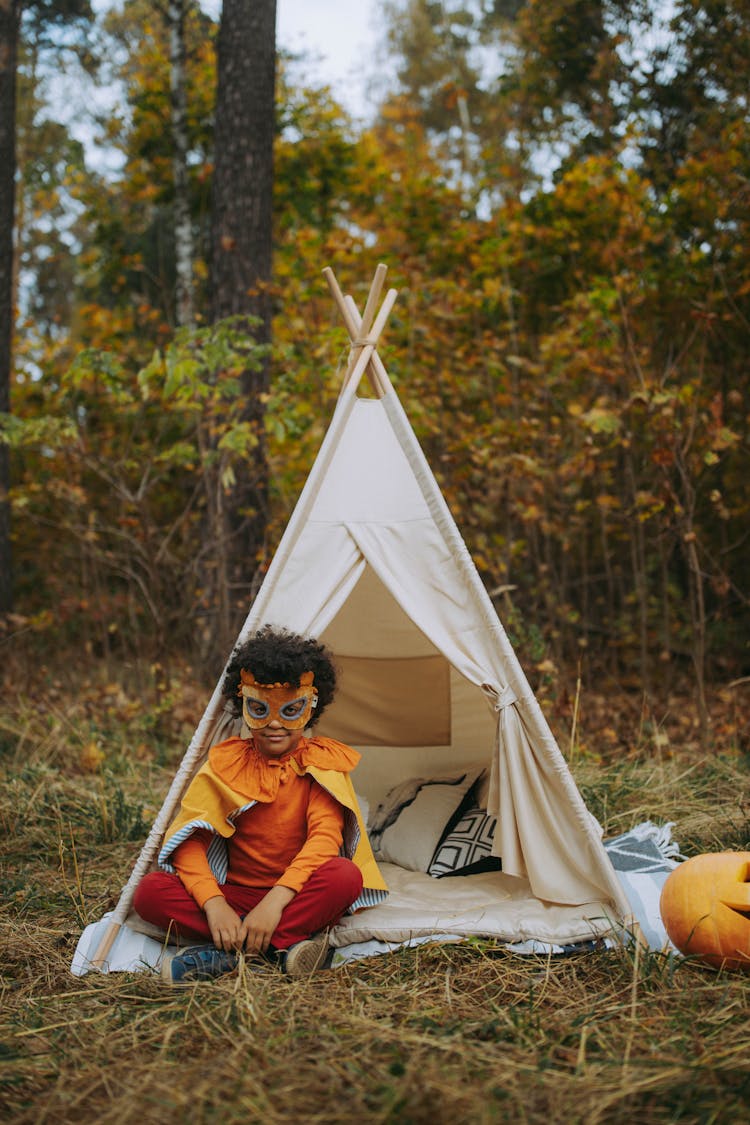 A Child In Costume Sitting Beside The Teepee