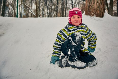 Free A happy child in colorful winter clothes sitting on snow in a forest setting. Stock Photo