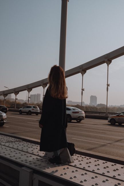 Back view of unrecognizable female in trendy wear standing on platform near post and city roadway in twilight
