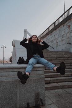 在城里的楼梯附近，一位穿着时髦、年轻愉快的女性倚着石头栅栏，一边拨弄着头发，一边享受着乐趣