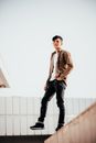 Man in Brown Leather Jacket and Black Denim Jeans Standing on White Concrete Wall