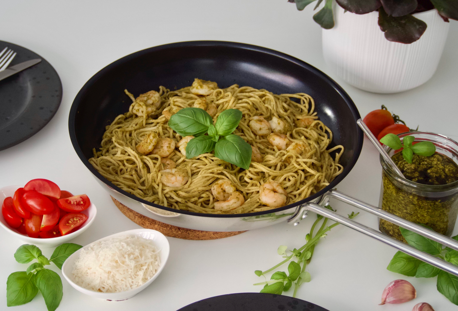 Appetizing shrimp pesto pasta in a skillet with fresh basil and parmesan on a white table.
