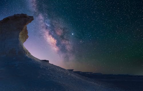 Spectacular landscape of rocky terrain under glowing sky with stars and galaxy at night