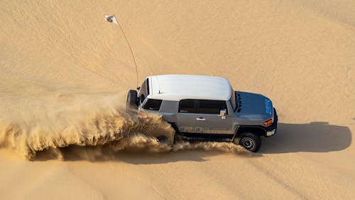 Modern SUV driving in sand of desert on hot day