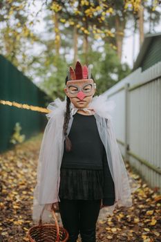 一个孩子穿着创意服装、戴着口罩，举着篮子站在户外绿树成荫的小路上