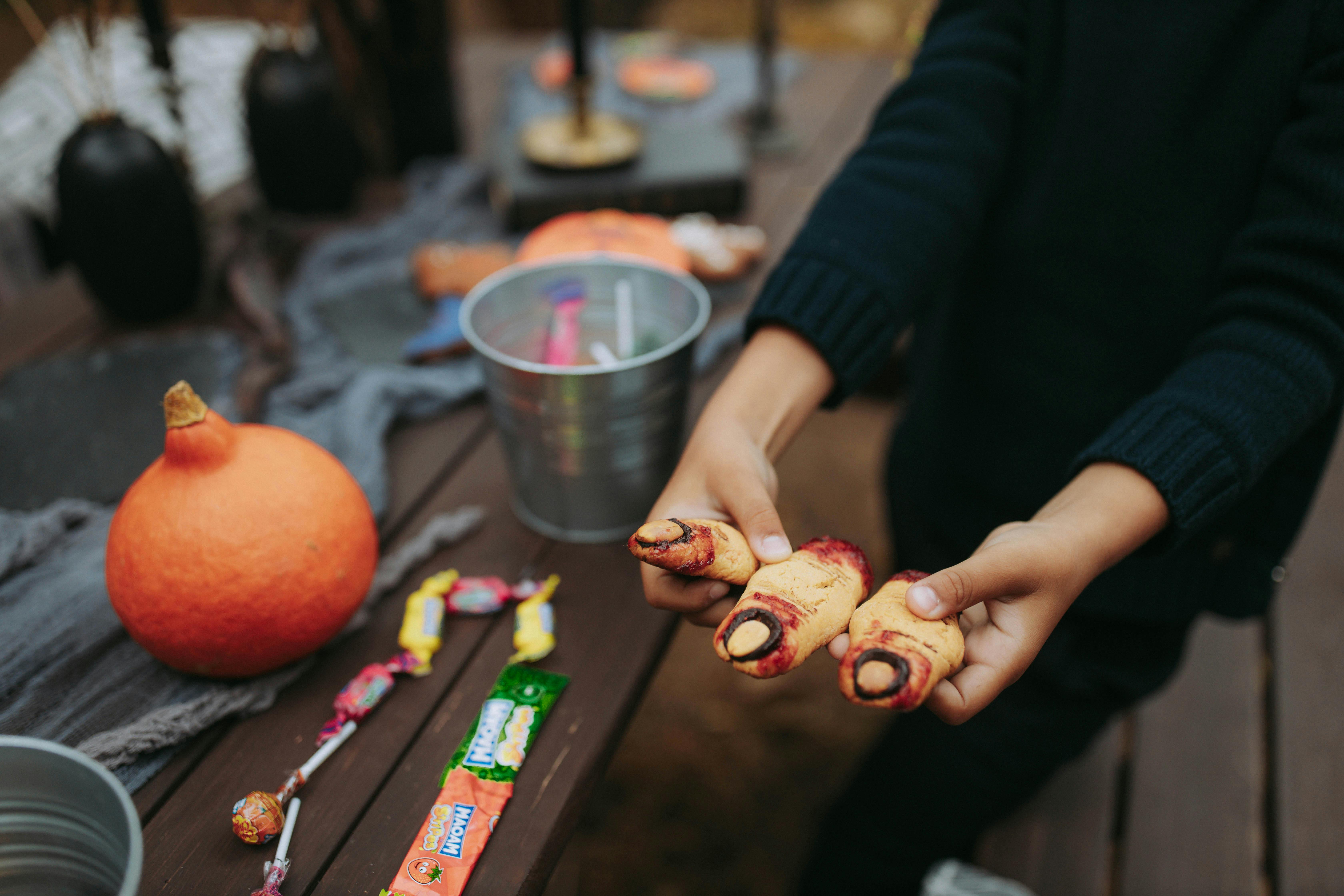 南瓜和糖果旁，一只手拿着怪异的万圣节手指形饼干特写