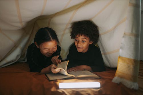 Children Reading a Book Under a Blanket