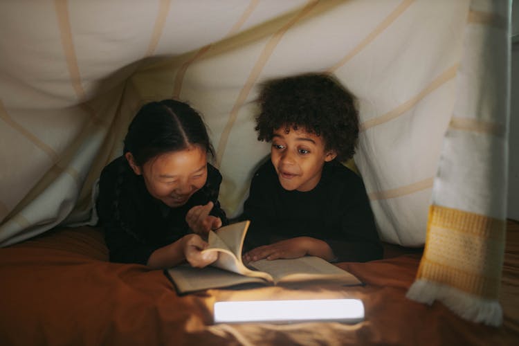 Children Reading A Book Under A Blanket