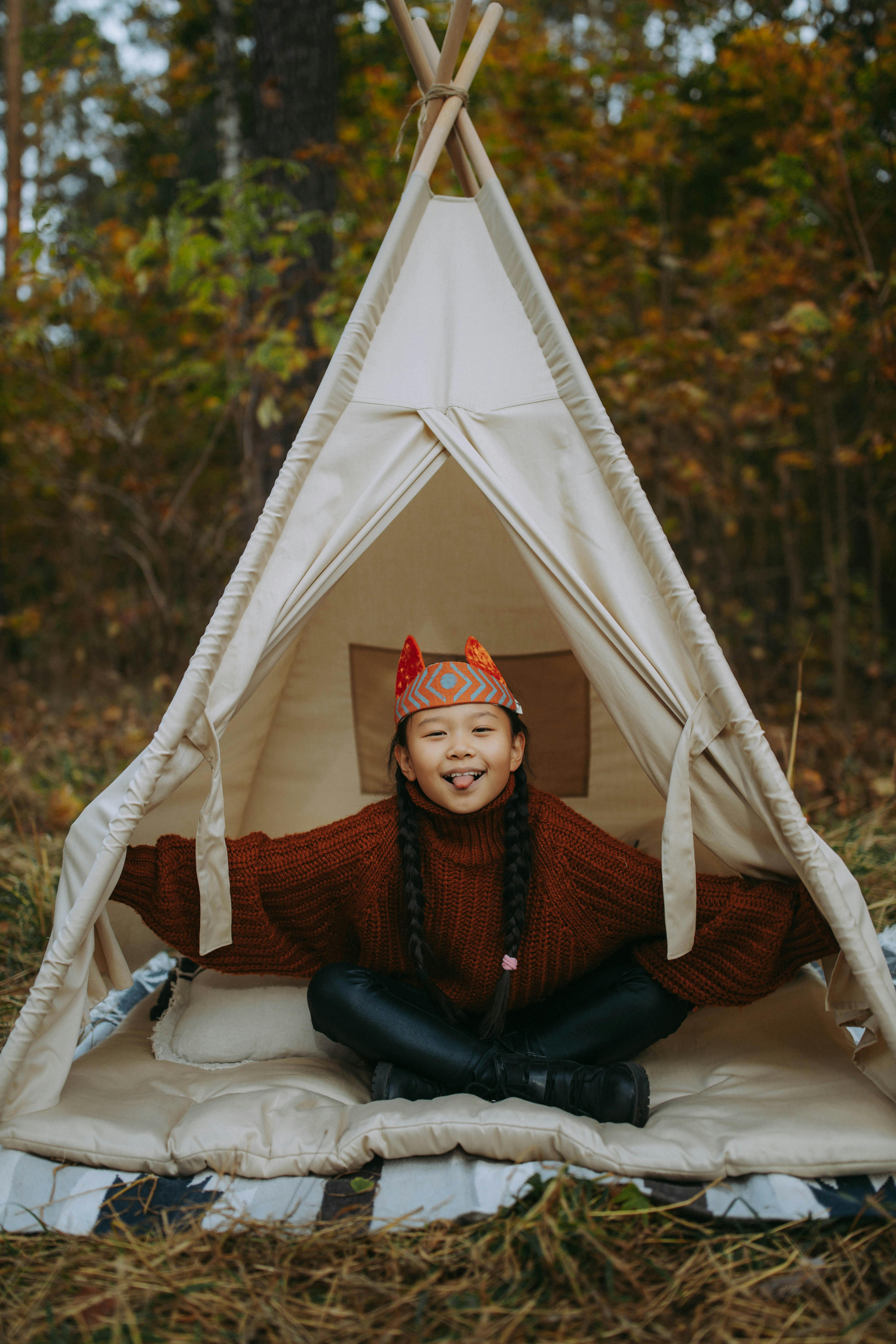 在秋天的背景下，一个穿着戏服的快乐女孩坐在户外的帐篷里