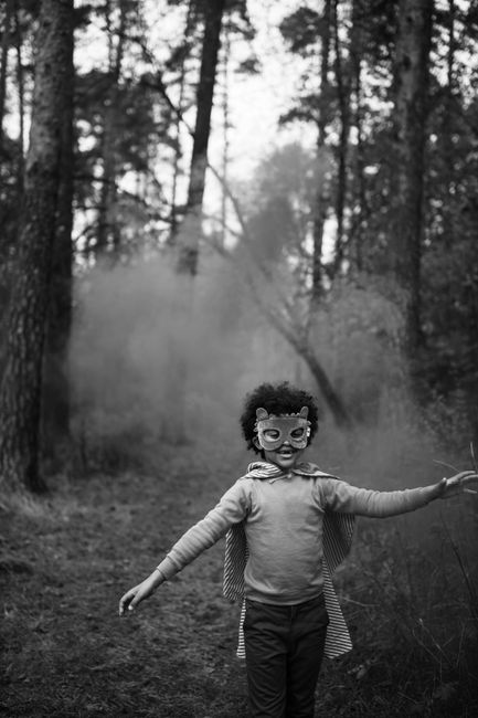A child wearing a mask enjoys a misty forest in black and white, embodying the Halloween spirit.