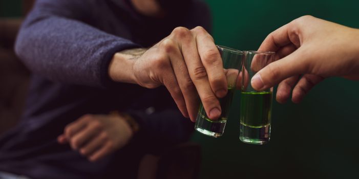 Two people clinking glasses of green drinks in a close-up shot, symbolizing celebration.